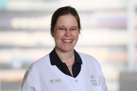 Barbara G&ouml;ring, eine l&auml;chelnde Frau mit Brille und wei&szlig;em Laborkittel, steht vor einem unscharfen Hintergrund. Sie hat ihr braunes Haar zur&uuml;ckgebunden und tr&auml;gt unter dem Laborkittel ein dunkles Hemd mit Kragen.