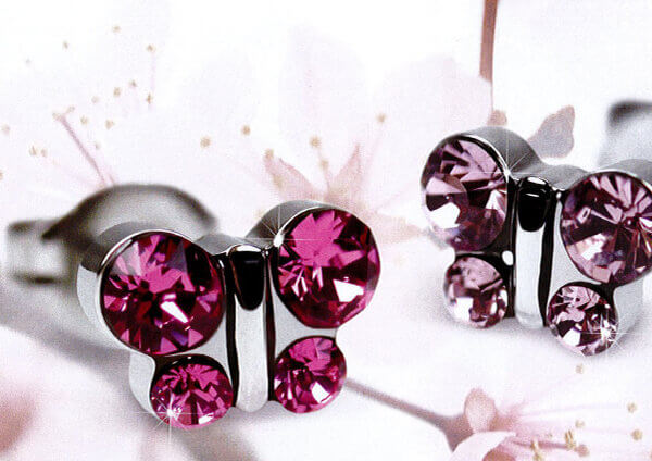 Ein Paar gl&auml;nzender silberner Ohrringe in Form eines Schmetterlings mit rosafarbenen Edelsteinen vor einem zarten Hintergrund mit hellrosa Kirschbl&uuml;ten.