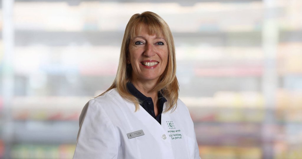 Gabriella Pagano, eine l&auml;chelnde Frau mit blondem Haar, tr&auml;gt einen wei&szlig;en Laborkittel und ein Namensschild, w&auml;hrend sie vor einem unscharfen Innenhintergrund steht.