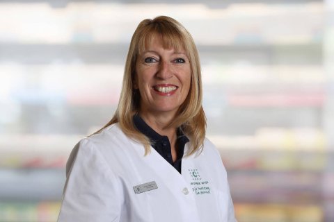 Gabriella Pagano, eine l&auml;chelnde Frau mit blondem Haar, tr&auml;gt einen wei&szlig;en Laborkittel und ein Namensschild, w&auml;hrend sie vor einem unscharfen Innenhintergrund steht.