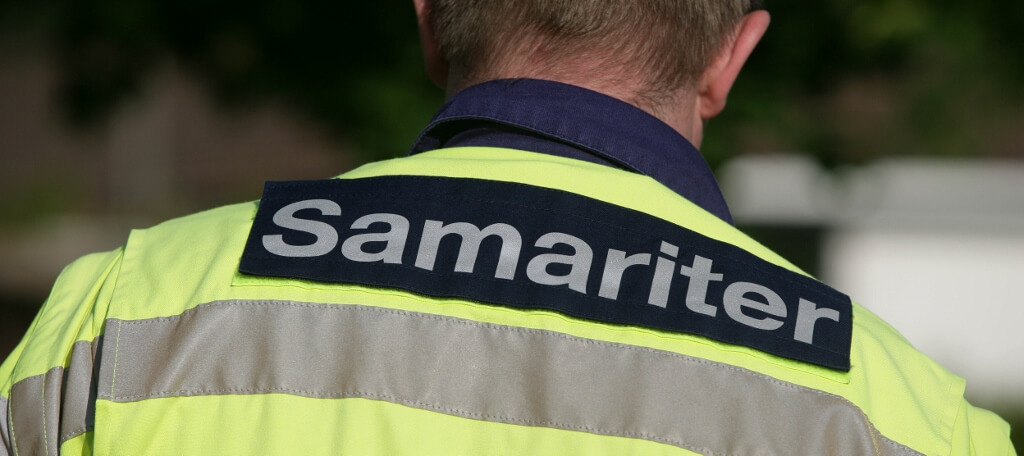 Eine Person, die von hinten zu sehen ist, trägt eine gelbe Warnweste mit reflektierenden Streifen und einem Aufnäher mit der Aufschrift Samariter auf dem Rücken, der für die örtlichen Samaritervereine steht.