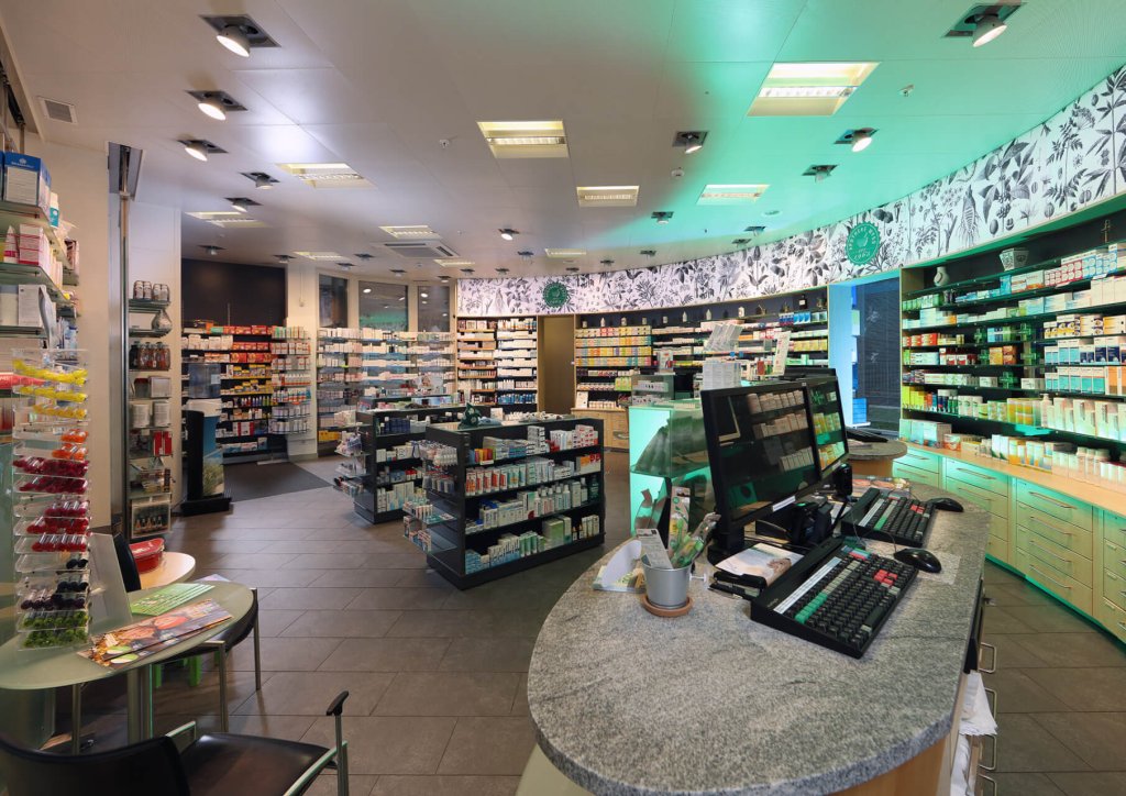 Eine moderne Apotheke mit Regalen mit Medikamenten und Gesundheitsprodukten, einer Theke mit Computerterminals im Vordergrund und heller, gut organisierter Beleuchtung und Einrichtung.