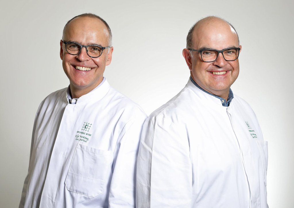 Zwei M&auml;nner mittleren Alters mit Brille und kurzen Haaren, beide in wei&szlig;en Laborkitteln, stehen nebeneinander und l&auml;cheln in die Kamera vor einem schlichten, hellen Hintergrund.