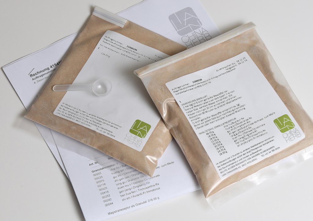 Zwei durchsichtige, mit braunem Pulver gef&uuml;llte Plastikbeutel, die jeweils mit Text und dem LA CHINA HERB-Logo beschriftet sind, stehen auf einer bedruckten Rechnung. Auf einem Beutel liegt eine kleine Schaufel, die die Bequemlichkeit des angebotenen TCM-Abholservices unterstreicht.