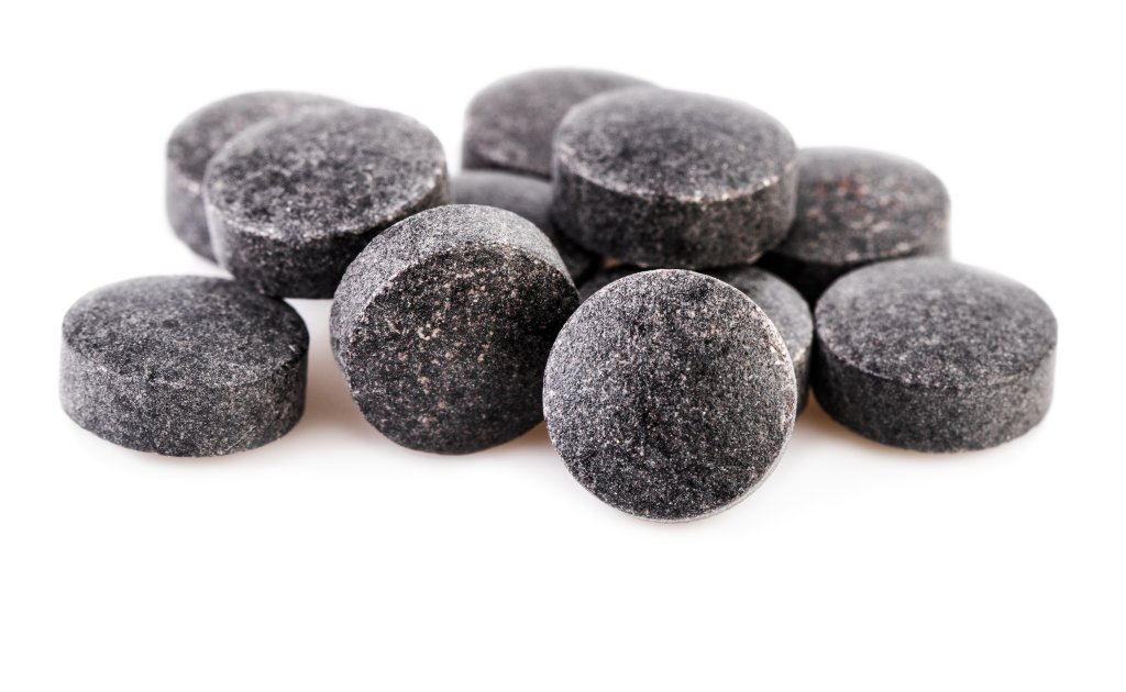 Eine Nahaufnahme mehrerer runder, schwarzer Tabletten, die auf wei&szlig;em Hintergrund aufeinander gestapelt sind und &uuml;blicherweise f&uuml;r Energiemangel oder einen niedrigen Energiestatus verwendet werden.