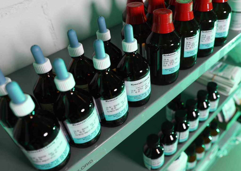 In einer Apotheke oder einem Labor reihen sich dunkle Glasflaschen mit wei&szlig;em Etikett und blauem oder rotem Verschluss, einschlie&szlig;lich Tropfer und Schraubverschl&uuml;sse, fein s&auml;uberlich in den Regalen auf und pr&auml;sentieren die korrekte Lagerung von Medikamenten.