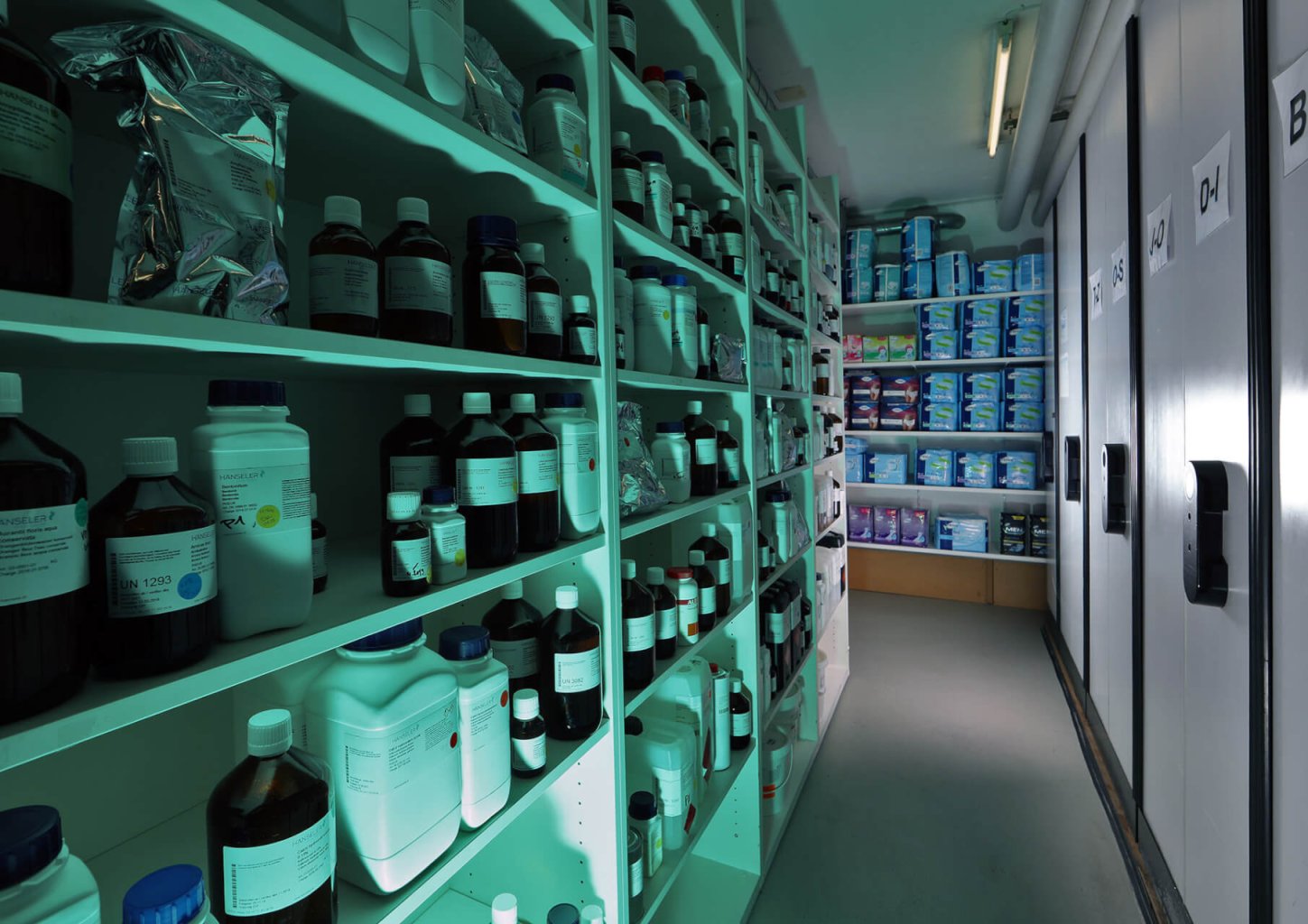 Die Regale in einem Lagerraum sind mit Flaschen, Beh&auml;ltern und Verpackungen von Chemikalien oder Laborbedarf gef&uuml;llt; blaues Licht beleuchtet den Raum und betont die korrekte Medikamentenlagerung in einer klinischen Atmosph&auml;re.