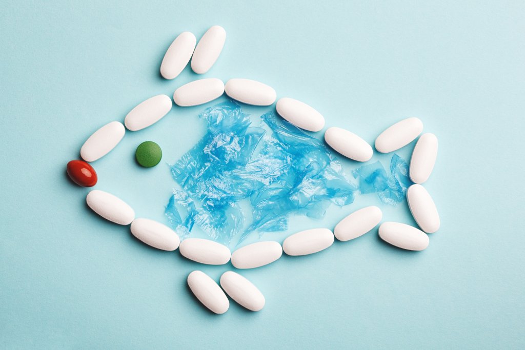 Eine Fischform wird mit wei&szlig;en Pillen als K&ouml;rper, einer roten Pille als Mund, einer gr&uuml;nen Pille als Auge und blauen Plastikst&uuml;cken im Inneren - die Antibiotikaresistenz visualisieren - auf einem hellblauen Hintergrund gestaltet.