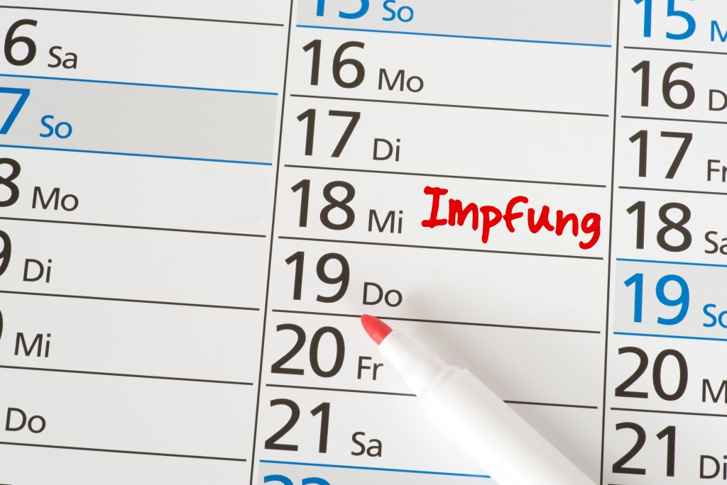 Nahaufnahme eines Kalenders mit dem Wort Impfung in roter Schrift am 18., das eine Grippeimpfung hervorhebt. Auf dem Kalender liegt ein roter Marker, dessen Kappe entfernt wurde.