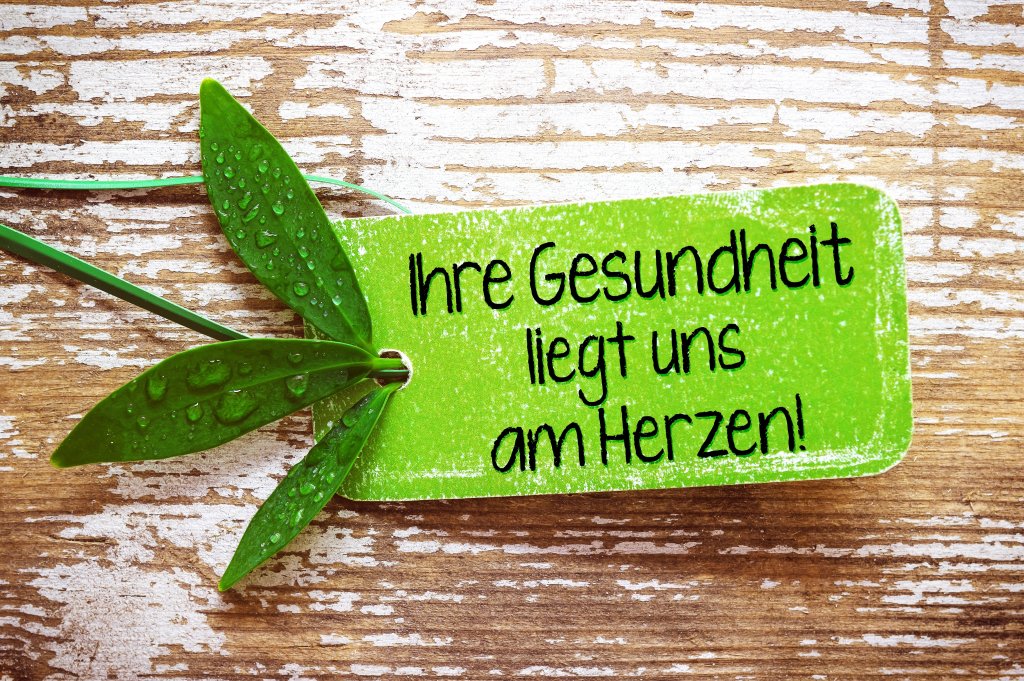 Ein gr&uuml;nes Schild mit Wassertropfen und Bl&auml;ttern mit der Aufschrift Ihre Gesundheit liegt uns am Herzen! auf einer rustikalen Holzoberfl&auml;che unterstreicht die Bedeutung von Gesundheit und Wohlbefinden - Ihre Gesundheit liegt uns am Herzen!.