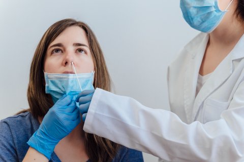 Eine medizinische Fachkraft, die Handschuhe und eine Maske tr&auml;gt, verabreicht einer Frau, die ihre Maske unter der Nase herunterzieht, einen Corona-Schnelltest-Nasenabstrich.