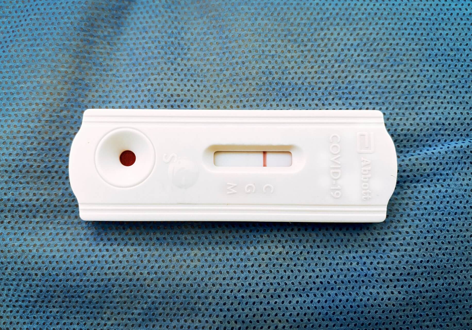 Eine Corona-Schnelltest-Kassette auf einer blau strukturierten Oberfl&auml;che zeigt eine einzelne rote Linie im Kontrollbereich, was auf ein negatives Ergebnis hinweist.