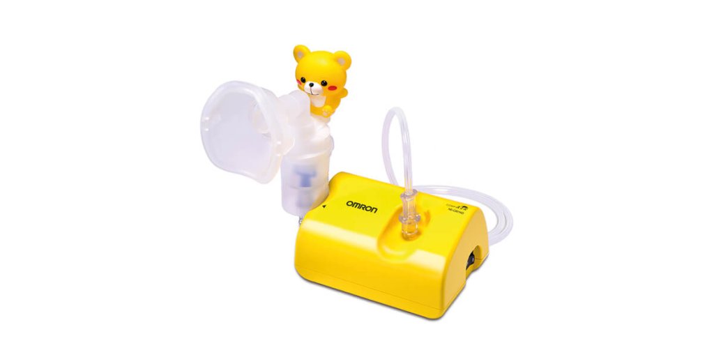 Ein gelber Omron Vernebler Sanit&auml;tsartikel mit einer durchsichtigen Maske und Schlauch, mit einer niedlichen B&auml;renfigur auf der Oberseite. Dieses Ger&auml;t ist speziell f&uuml;r Kinder konzipiert und sitzt auf einem wei&szlig;en Hintergrund.