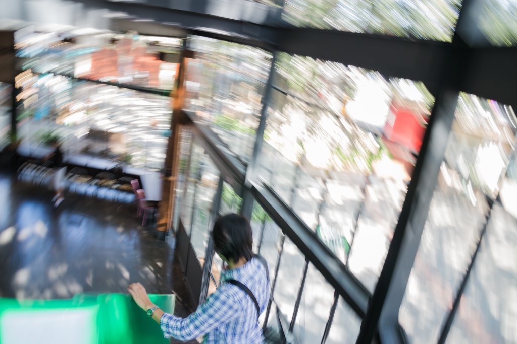 Eine Person in einem karierten Hemd geht eine hell erleuchtete Treppe hinunter, die von Glasfenstern umgeben ist; das Bild ist unscharf und vermittelt ein Gef&uuml;hl von Bewegung und Schwindel.