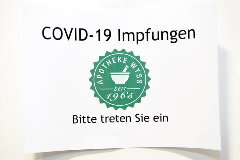Ein Schild mit der Aufschrift COVID-19 Impfungen, darunter das Logo der Apotheke Wyss und der Text Bitte treten Sie ein und laden Ihren Besuch ein. DGS-Informationen k&ouml;nnen auch f&uuml;r die Zug&auml;nglichkeit verf&uuml;gbar sein.