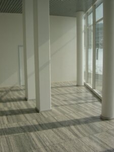 Ein leerer, moderner Innenraum mit gro&szlig;en Fenstern, wei&szlig;en S&auml;ulen und Marmorb&ouml;den. Das Sonnenlicht str&ouml;mt durch die Fenster und wirft Schatten auf den Boden. Draussen ist Schnee zu sehen - eine elegante Kulisse im T&auml;fernhof D&auml;ttwil, perfekt f&uuml;r ein 15-j&auml;hriges Jubil&auml;um.