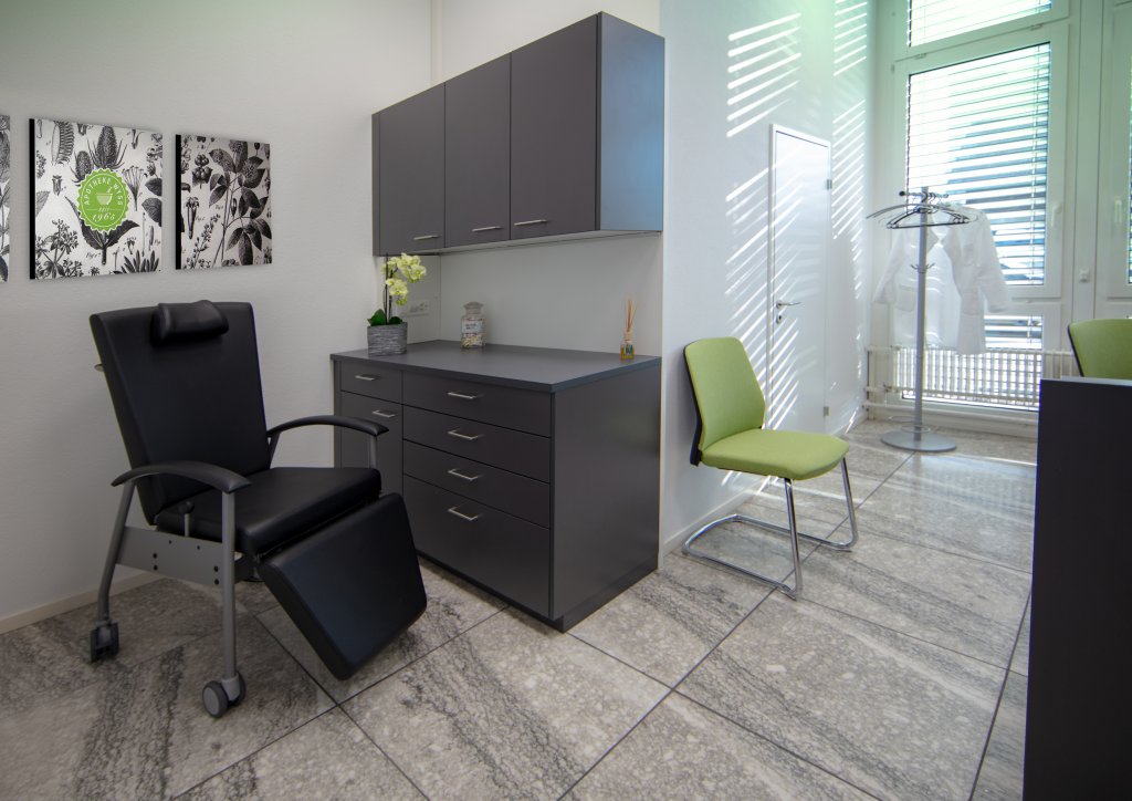 Ein modernes medizinisches B&uuml;ro am Standort D&auml;ttwil verf&uuml;gt &uuml;ber einen schwarzen Untersuchungsstuhl, graue Schr&auml;nke, gr&uuml;ne St&uuml;hle, Wandkunst, eine kleine Pflanze und einen Kleiderst&auml;nder an einem gro&szlig;en Fenster, das viel Tageslicht hereinl&auml;sst.