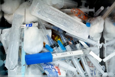 Nahaufnahme eines Haufens gebrauchter medizinischer Spritzen, Watteb&auml;llchen, Plastikverpackungen und Fl&auml;schchen, die alle zusammen in einem Beh&auml;lter f&uuml;r die ordnungsgem&auml;&szlig;e Medikamenten-Entsorgung entsorgt werden.