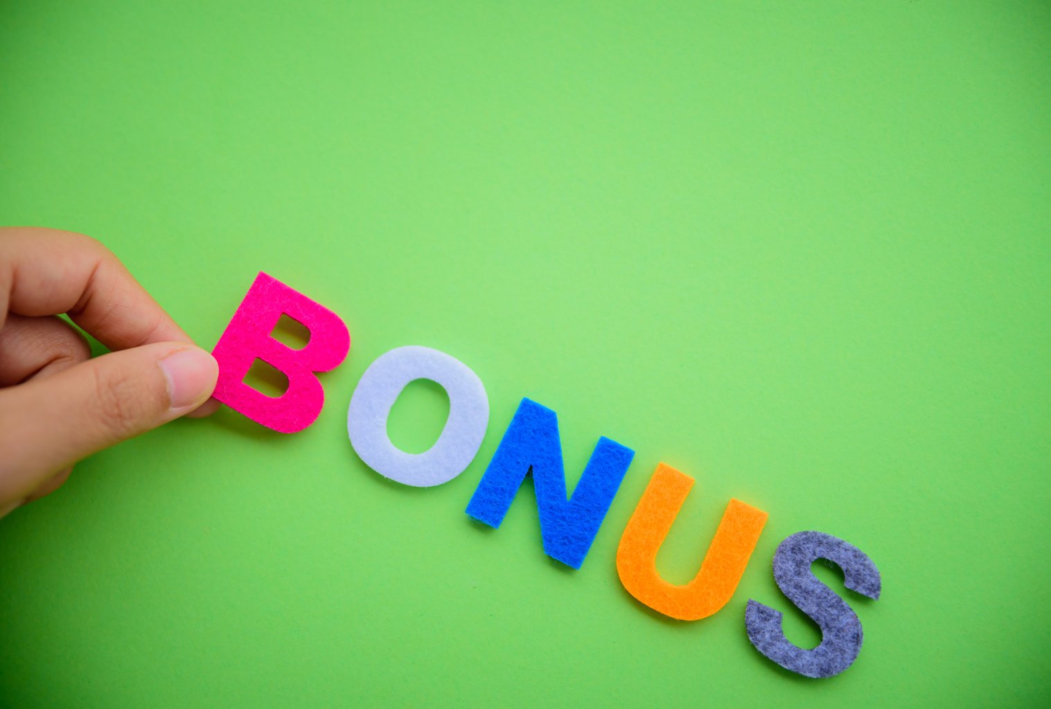 Eine Hand h&auml;lt den rosafarbenen Buchstaben B in dem Wort BONUS, das mit bunten Filzbuchstaben auf einem leuchtend gr&uuml;nen Hintergrund geschrieben ist - perfekt f&uuml;r die Darstellung von Sammelkarten-Belohnungen.
