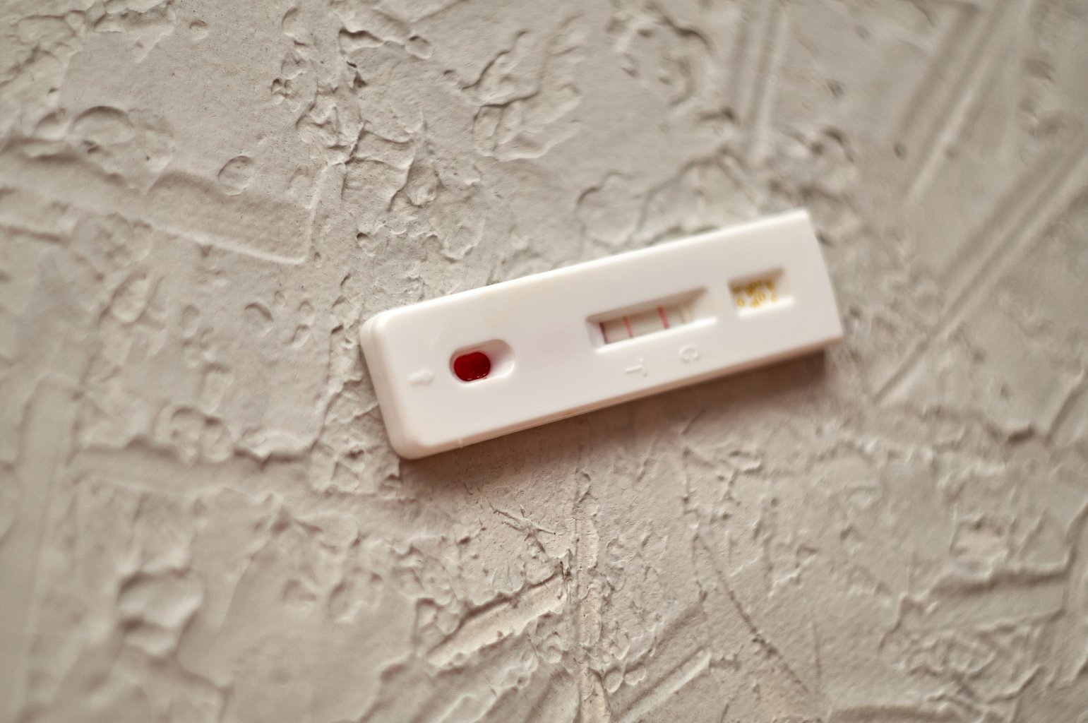 Eine wei&szlig;e Schnelltestkassette mit zwei sichtbaren roten Linien liegt auf einer strukturierten, hellen Oberfl&auml;che und zeigt ein positives Ergebnis an.