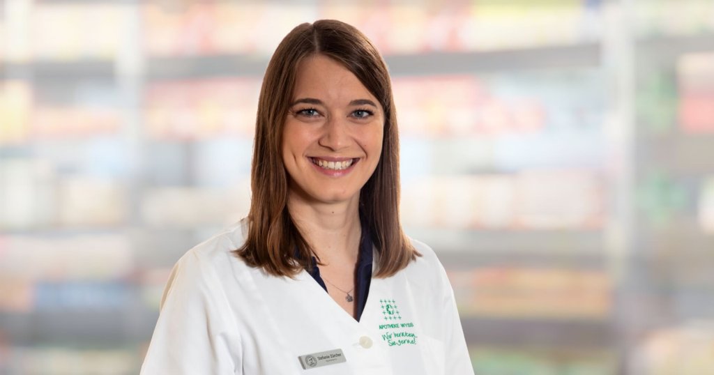 Stefanie Z&uuml;rcher, eine Frau mit glattem braunem Haar und wei&szlig;em Laborkittel, l&auml;chelt in die Kamera. Der Hintergrund ist unscharf, mit weichen Farben und undeutlichen Formen, die auf einen Innenraum hindeuten.