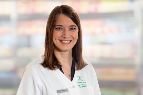 Stefanie Z&uuml;rcher, eine Frau mit glattem braunem Haar und wei&szlig;em Laborkittel, l&auml;chelt in die Kamera. Der Hintergrund ist unscharf, mit weichen Farben und undeutlichen Formen, die auf einen Innenraum hindeuten.