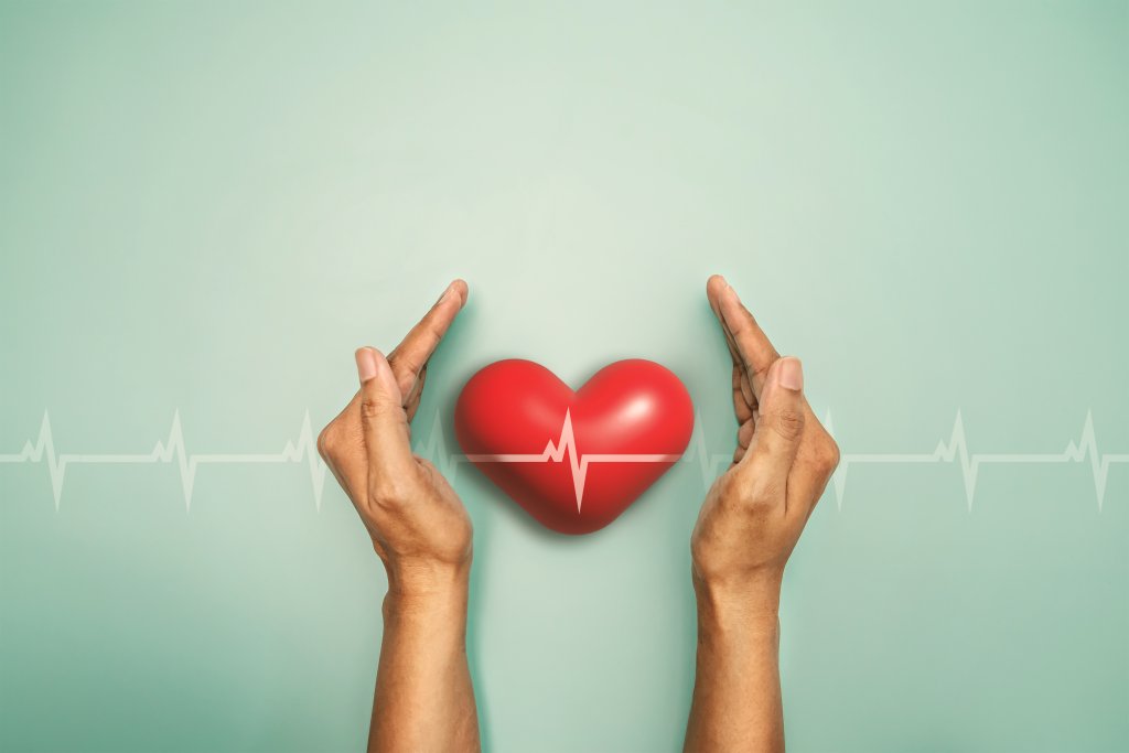 Zwei Zeiger umgeben ein rotes Herz mit einer wei&szlig;en EKG-Herzschlaglinie, die Gef&auml;sse und die Wichtigkeit der &Uuml;berwachung des Hohen Blutdrucks symbolisiert, vor einem hellen tealfarbenen Hintergrund mit zus&auml;tzlichen Herzschlaglinien.