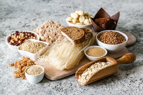 Eine Vielzahl von glutenfreien Lebensmitteln f&uuml;r Menschen mit Glutenunvertr&auml;glichkeit oder Z&ouml;liakie, darunter Reisnudeln, Schwarzbrot, Bohnen, Hafer, Buchweizen, Hirse, Puffreiskuchen, Gnocchi und Muffins - h&uuml;bsch angerichtet auf Holzbrettern und in Schalen.