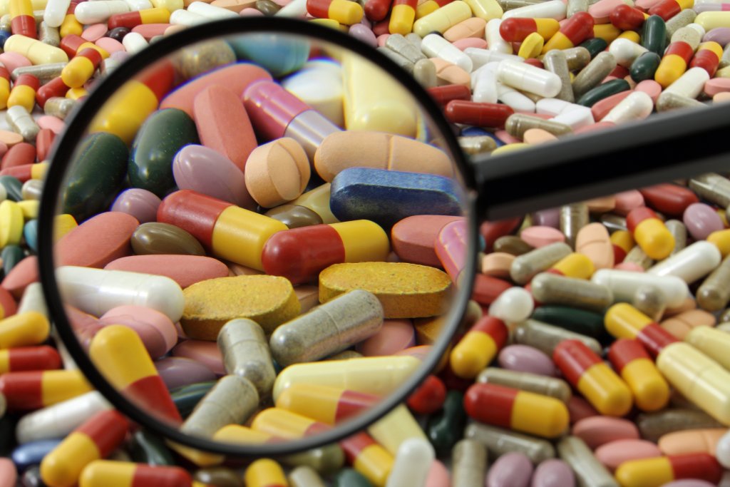 Ein Vergr&ouml;&szlig;erungsglas schwebt &uuml;ber einem Stapel bunter Pillen und Kapseln und hebt einige Tabletten in den vielen verschiedenen Formen und Farben der Medikamente n&auml;her hervor.