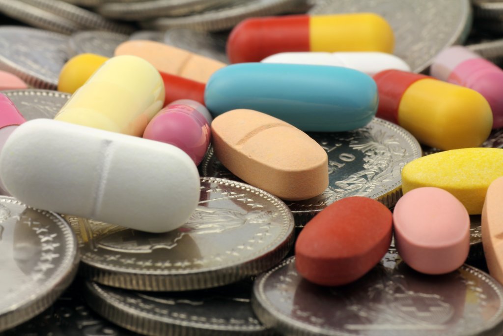 Verschiedene bunte Pillen und Kapseln, die auf mehreren Silberm&uuml;nzen verstreut sind, symbolisieren die Kosten f&uuml;r Medikamente, die Krankenkassen-Pr&auml;mien 2024 und die Bedeutung von Sparen f&uuml;r Gesundheit.