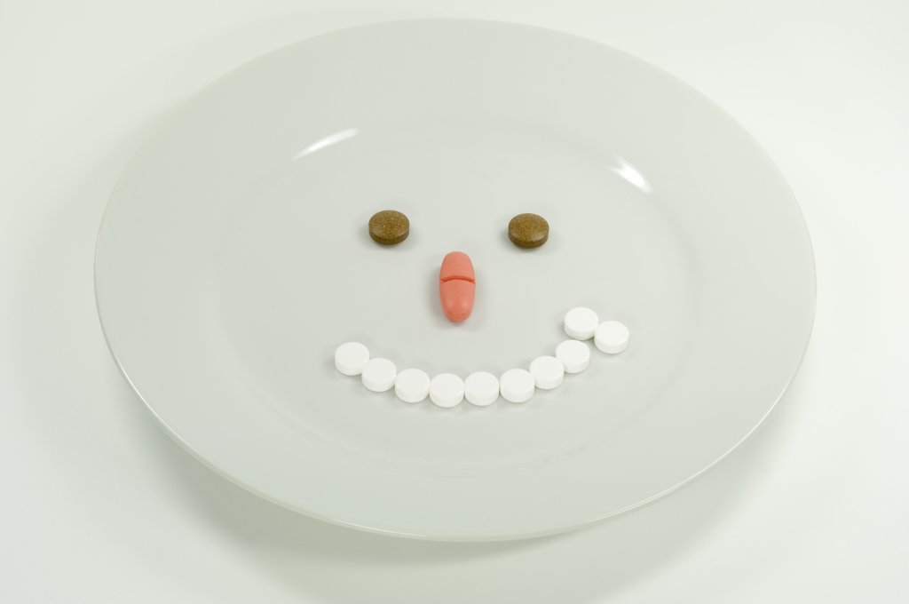 Ein wei&szlig;er Teller mit Pillen, die so angeordnet sind, dass sie ein l&auml;chelndes Gesicht bilden: zwei braune Pillen f&uuml;r die Augen, zwei rosafarbene Pillen f&uuml;r die Nase und mehrere wei&szlig;e runde Pillen, die ein geschwungenes L&auml;cheln bilden - ein Symbol f&uuml;r eine wirkungsvolle Medikamenteneinnahme.