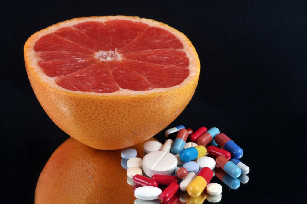 Eine halbierte Grapefruit liegt neben einem gemischten Stapel bunter Pillen und Tabletten auf einer schwarzen, spiegelnden Oberfl&auml;che und unterstreicht die Bedeutung der korrekten Medikamenteneinnahme.