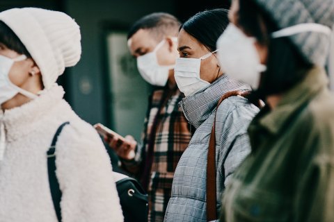 Eine Gruppe von Personen mit Gesichtsmasken und Winterkleidung steht im Herbst 2024 im Freien dicht beieinander und wartet m&ouml;glicherweise auf ihre COVID-19-Impfung. Der Hintergrund ist unscharf und lenkt den Blick auf die bedeckten Gesichter und die Schutzausr&uuml;stung.