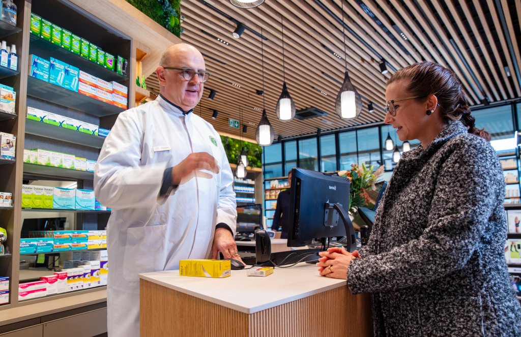 Ein Apotheker im weissen Kittel spricht mit einer Frau am Schalter der Apotheke Wyss. Die Frau h&ouml;rt aufmerksam zu. Auf dem Tresen stehen Medikamentenschachteln, Regale mit Gesundheitsprodukten f&uuml;llen die modern gestaltete Bahnhof-Apotheke Baden.