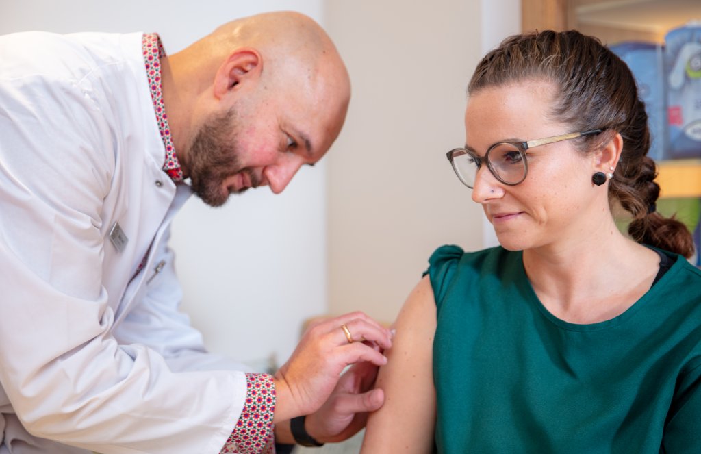 In der Apotheke Wyss, modern gestaltet in der N&auml;he des Bahnhofs Baden, verabreicht eine medizinische Fachkraft im weissen Kittel einer Frau mit Brille und gr&uuml;nem &auml;rmellosen Oberteil eine Impfstoffspritze. Sie schaut w&auml;hrend des Eingriffs ruhig weg.