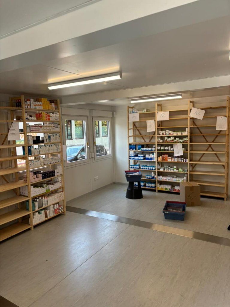 Eine modern gestaltete Apotheke Wyss in der N&auml;he des Bahnhofs Baden mit Regalen mit Medikamentenschachteln und Flaschen, beschrifteten F&auml;chern, einem Hocker, Kartons und Beh&auml;ltern auf dem Boden und grossen Fenstern, die den Raum mit nat&uuml;rlichem Licht f&uuml;llen.