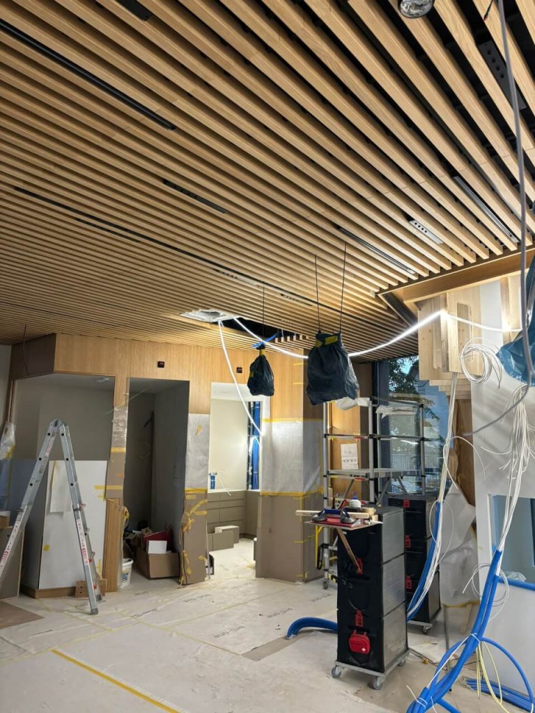 Ein modernes, im Bau befindliches Interieur im Bahnhof Baden mit einer Holzlattendecke, Leitern, Werkzeugen und Baumaterialien, die verstreut herumliegen. Von der Decke h&auml;ngen Dr&auml;hte und Rohre, und Teile des Raums bei der Apotheke Wyss sind zum Schutz abgeklebt.