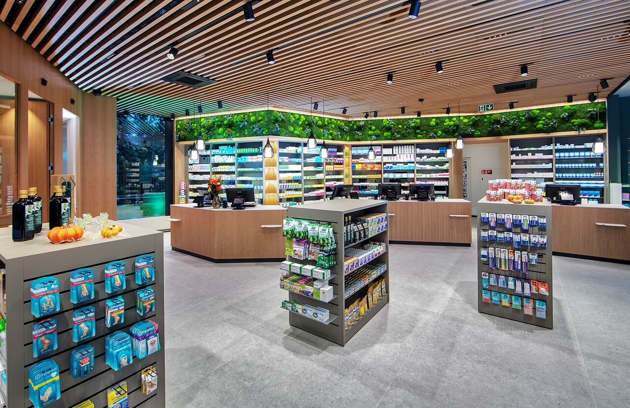 Modernes Apothekeninterieur in der Apotheke Wyss beim Bahnhof Baden mit Holzdecken, hellen Regalen mit Medikamenten und Gesundheitsprodukten, Gr&uuml;npflanzen an der R&uuml;ckwand und grossz&uuml;gigen Auslagen f&uuml;r rezeptfreie Artikel.