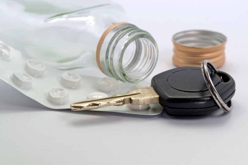 Ein Autoschl&uuml;ssel und eine Blisterpackung mit Medikamenten liegen neben einer ge&ouml;ffneten, leeren Glasflasche ohne Verschluss auf einer wei&szlig;en Fl&auml;che und werfen Fragen zur Fahrt&uuml;chtigkeit auf.