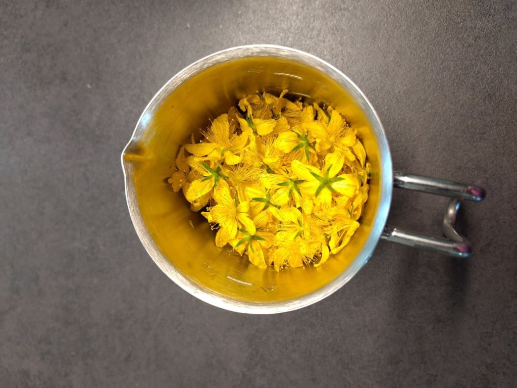 Ein Metallbeh&auml;lter, gef&uuml;llt mit frisch gepfl&uuml;ckten gelben Blumen, steht auf einer dunkelgrauen Fl&auml;che, von oben betrachtet.