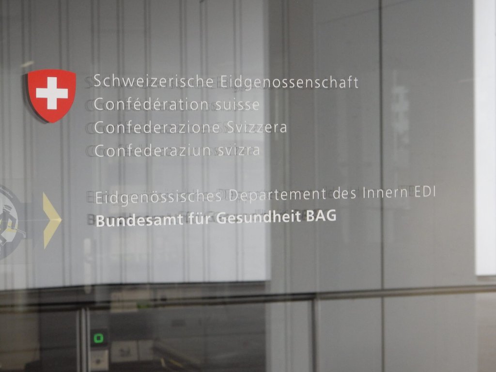 Glast&uuml;r mit Schweizer Wappen und mehrsprachigem Text f&uuml;r das Bundesamt f&uuml;r Gesundheit (BAG), der auf die Neuen Medikamentenpreise und die LOA V 2026 hinweist - wichtige Aktualisierungen f&uuml;r jede Apotheke.