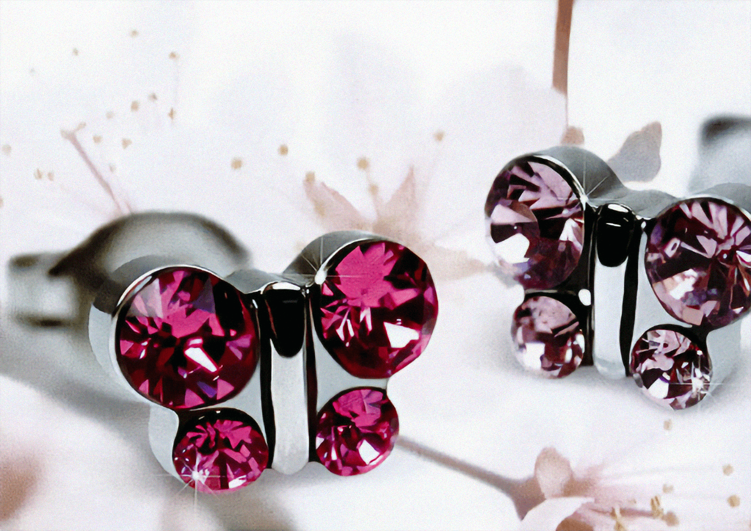 Eine Nahaufnahme von zwei silbernen schmetterlingsf&ouml;rmigen Ohrringen mit rosa und lila Edelsteinen vor einem weichen, verschwommenen Hintergrund mit wei&szlig;en und rosa Blumen.
