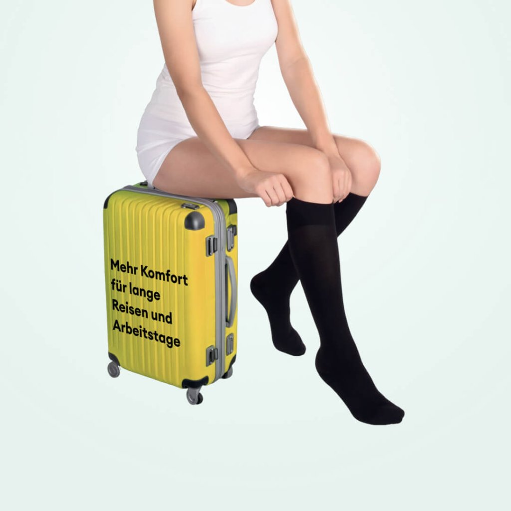 Eine Frau in weißer Kleidung sitzt auf einem gelben Koffer mit der Aufschrift „Mehr Komfort für lange Reisen und Arbeitstage“ und trägt schwarze Kompressionsstrümpfe für „leichte Beine beim Reisen“.